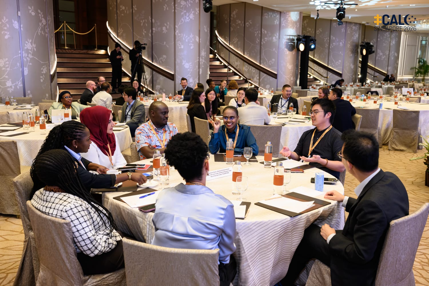 Delegates engaged in discussion around a round table in the ballroom at The Fullerton Hotel Singapore during a networking session at the Conference.